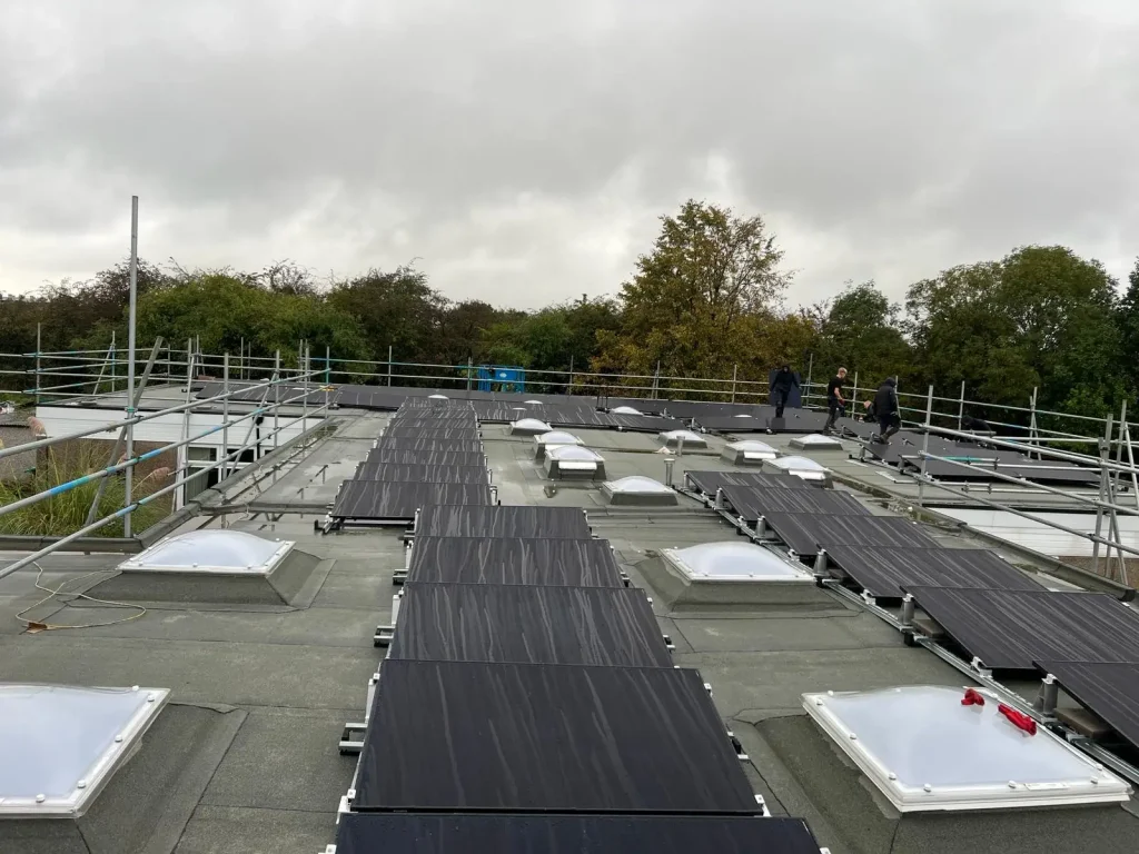 Flat rooftop solar panel installation in progress with scaffolding, skylights, and three workers on site