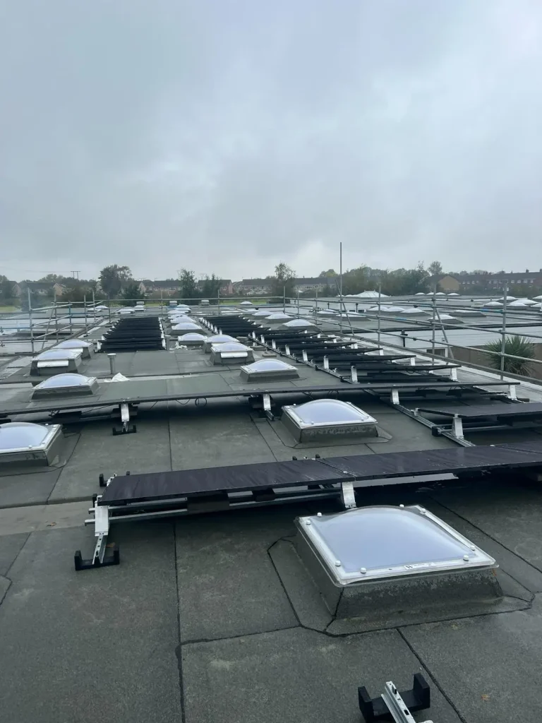 Flat rooftop with rows of solar panels mounted on metal frames and multiple dome-shaped skylights
