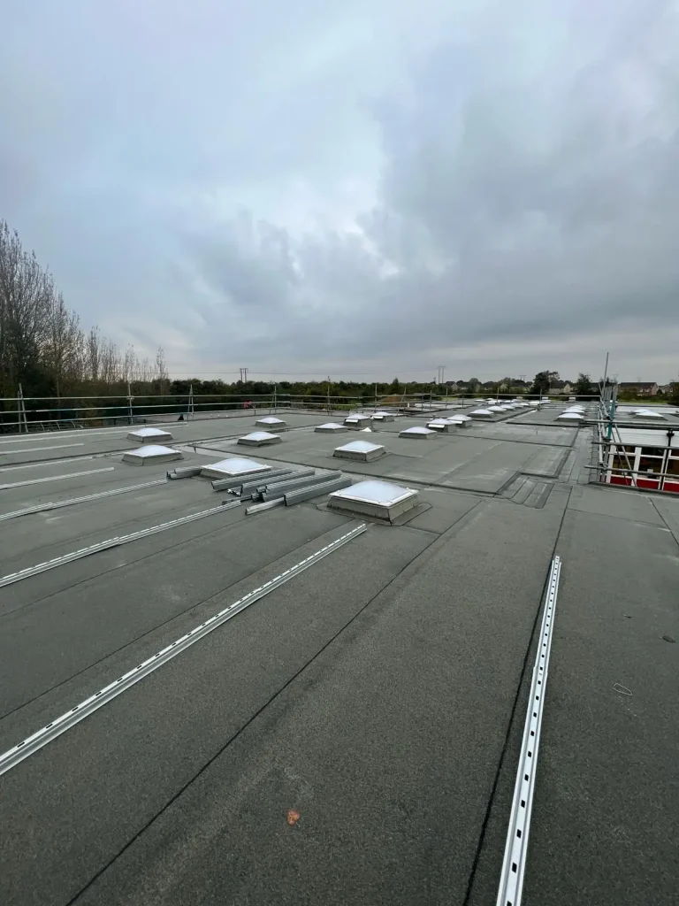 Flat rooftop with rectangular skylights, metal rails and piping laid out for installation