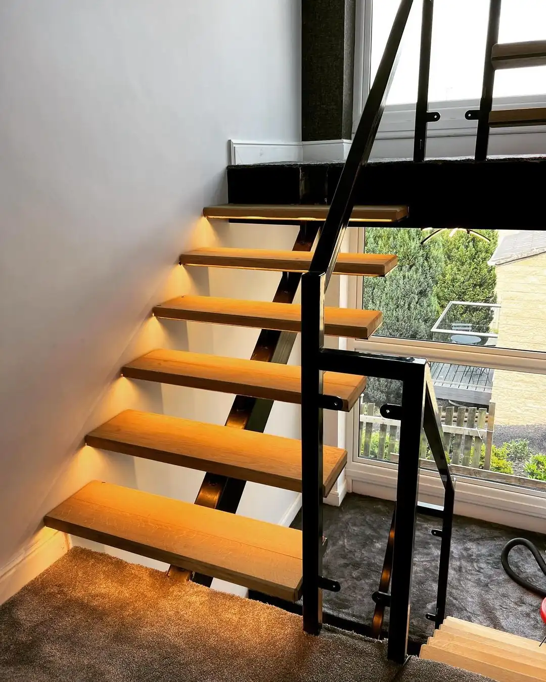 Staircase with wooden steps, black metal railings, and under-step lighting