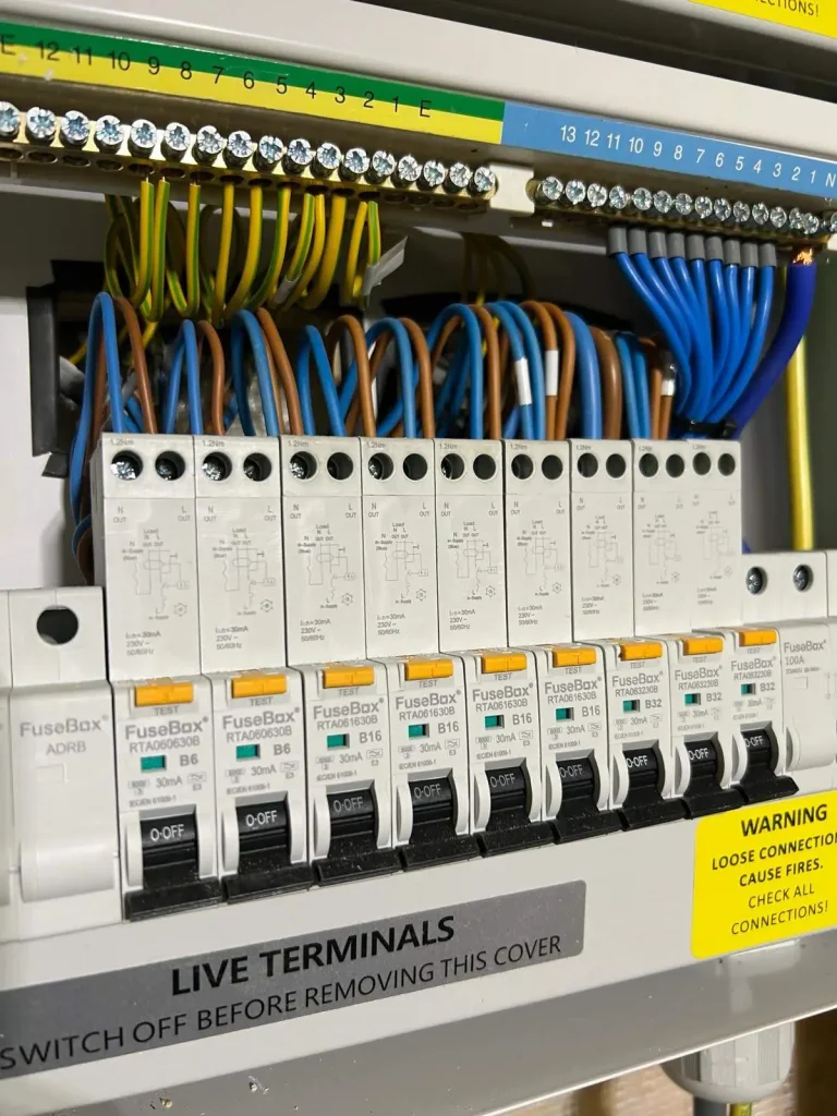 Electrical fuse box with labeled circuit breakers, colored wiring, and safety warnings about live terminals and fire risk