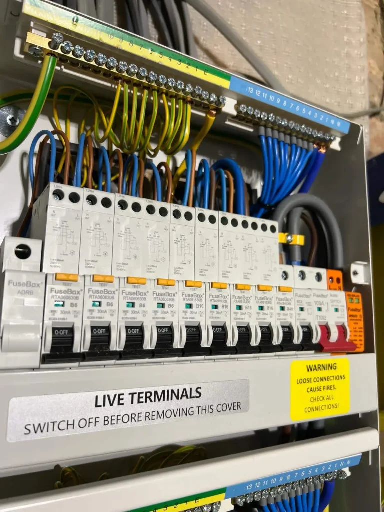 Electrical fuse box with labeled circuit breakers, colored wiring, and safety warnings about live terminals and fire risk
