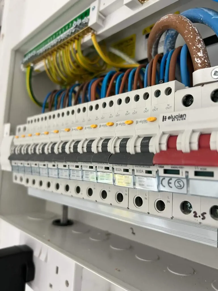 Electrical fuse box with labeled circuit breakers, colored wiring, and safety warnings about live terminals and fire risk