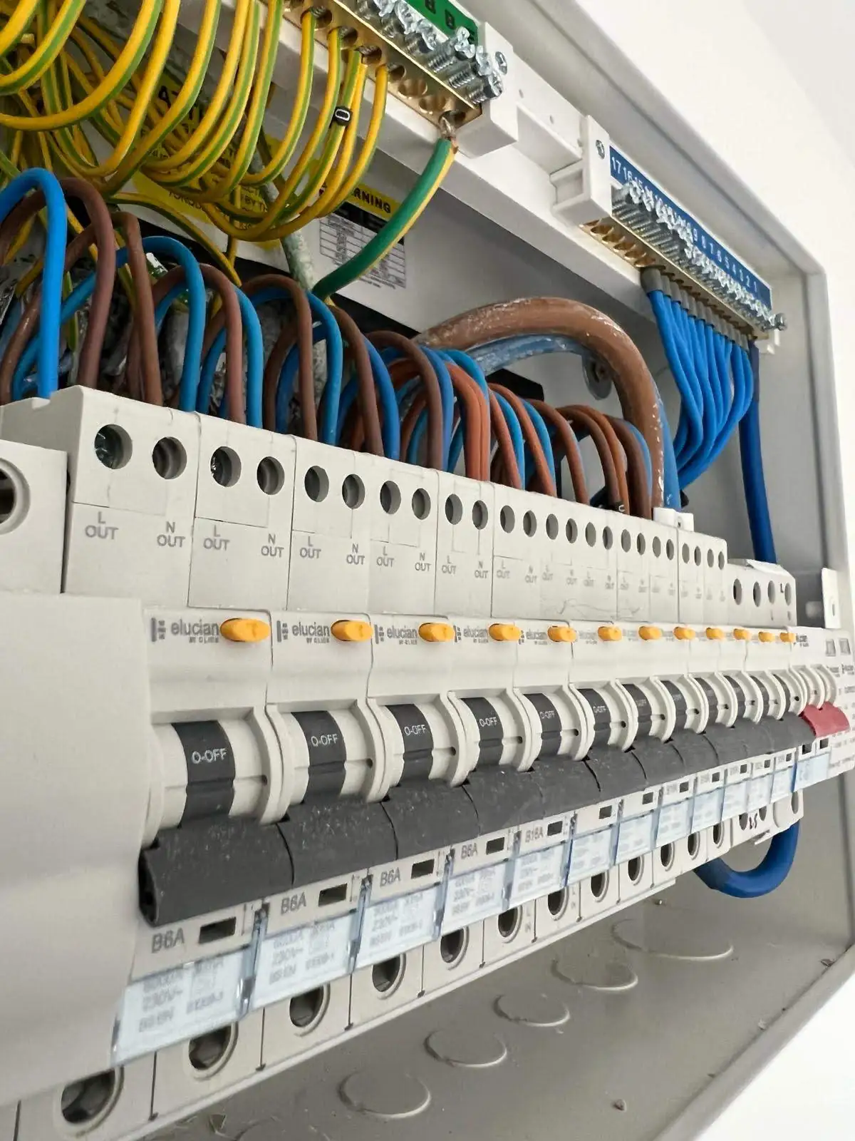 Electrical fuse box with labeled circuit breakers, colored wiring, and safety warnings about live terminals and fire risk