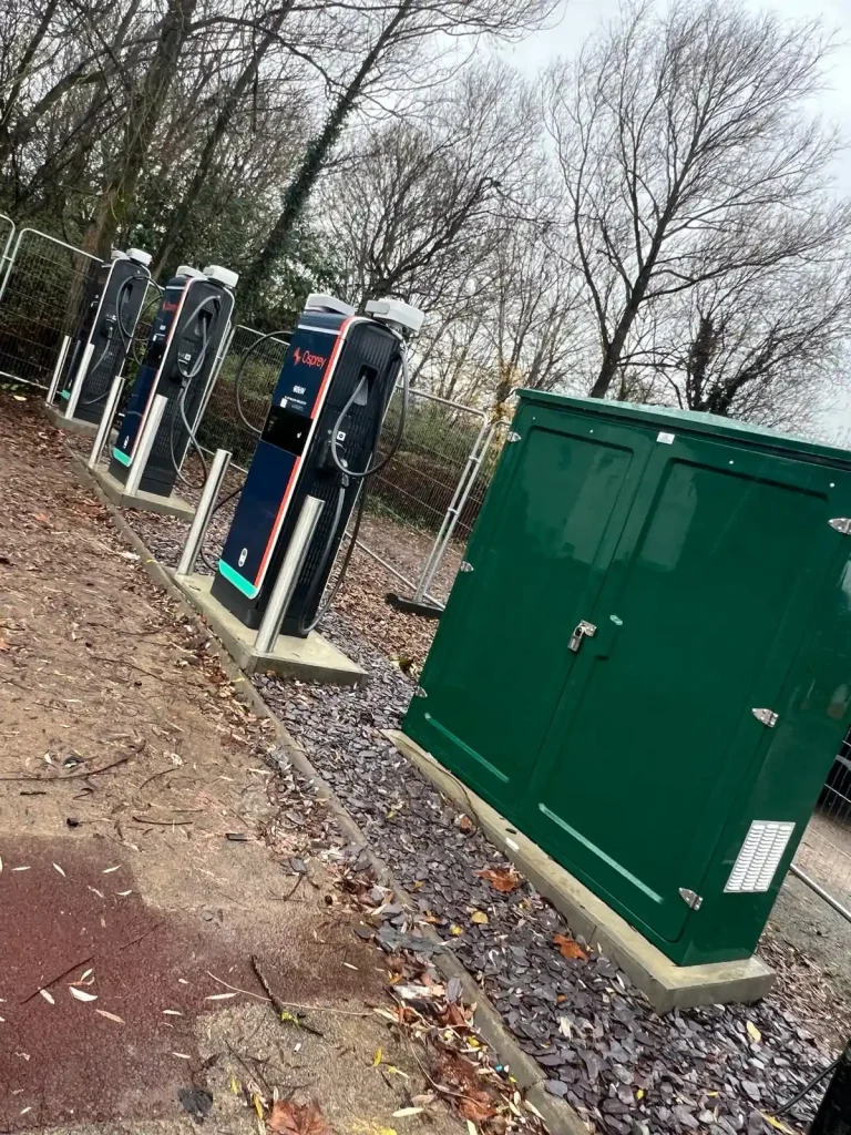 Three Osprey-branded EV charging stations with cables and connectors, installed on concrete surface beside green utility box