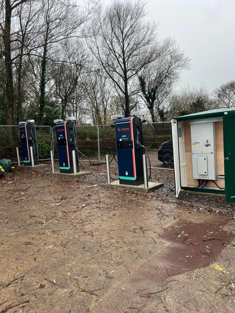 Three Osprey-branded EV charging stations with cables and connectors, installed on concrete surface beside green utility box