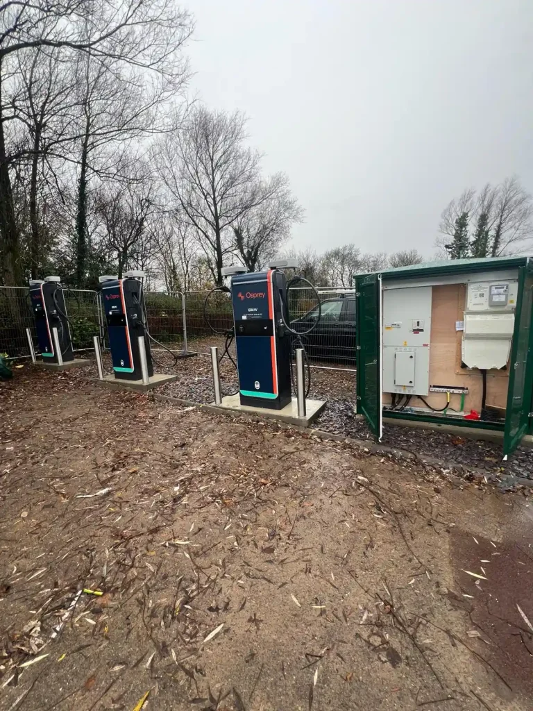 Three Osprey-branded EV charging stations with cables and connectors, installed on concrete surface beside green utility box