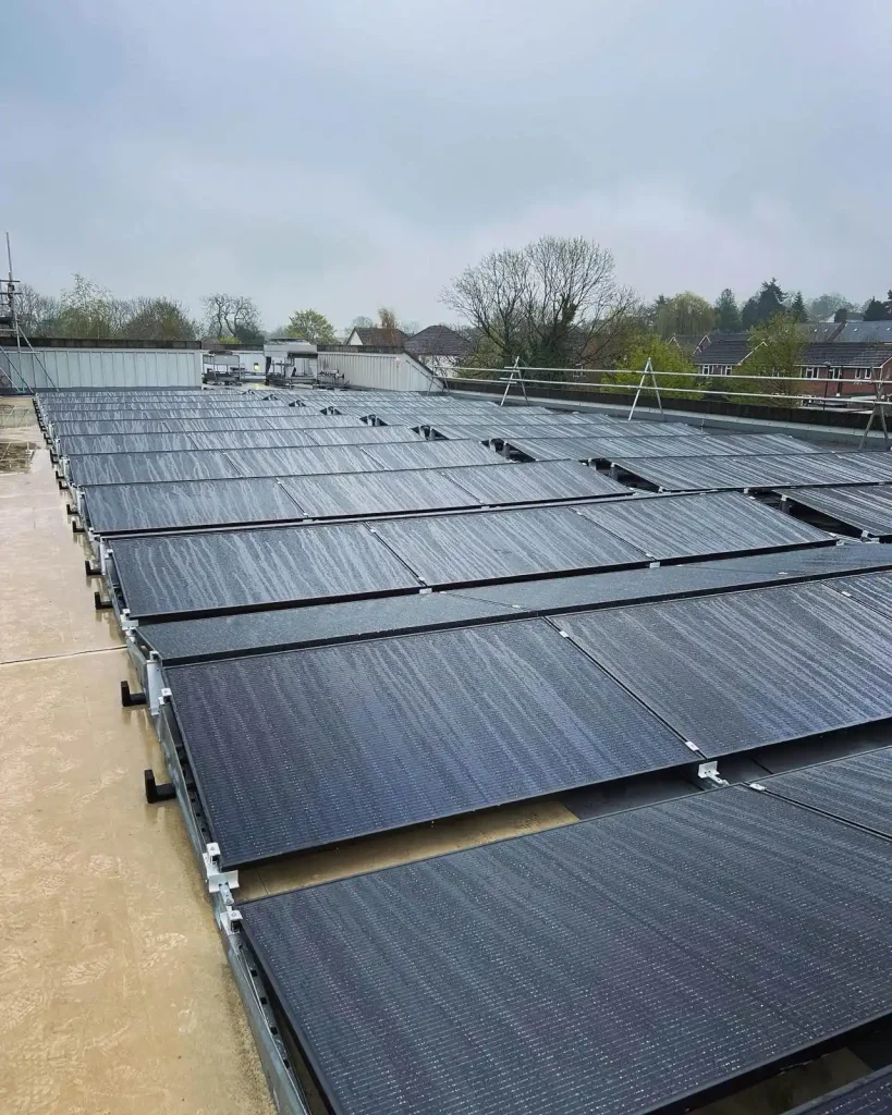 Flat rooftop solar panel array with multiple tilted rows and a wet surface from recent rain