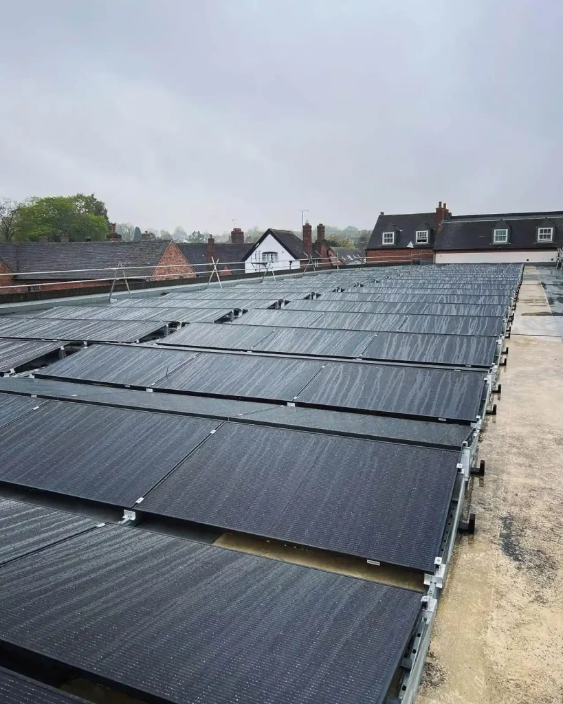 Flat rooftop solar panel array with multiple tilted rows and a wet surface from recent rain