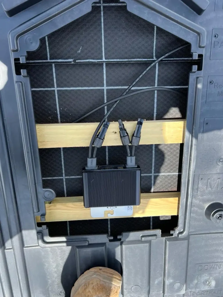 Close-up of solar panel rear side with junction box and connectors, mounted on wooden support bar